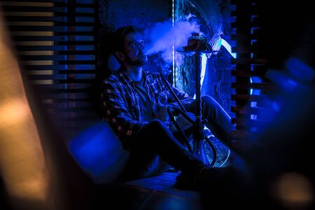 young guy smokes hookah in neon light barの写真素材