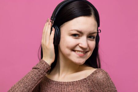 Image of a happy young beautiful woman posing isolated over pink wall background listening music with earphonesの写真素材