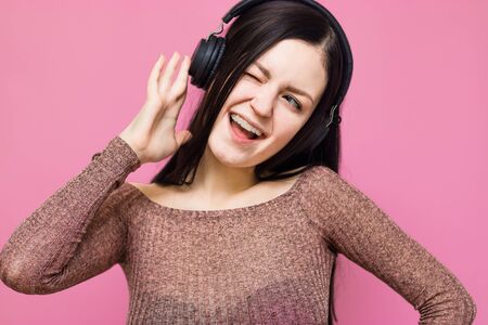 Image of a happy young beautiful woman posing isolated over pink wall background listening music with earphonesの写真素材