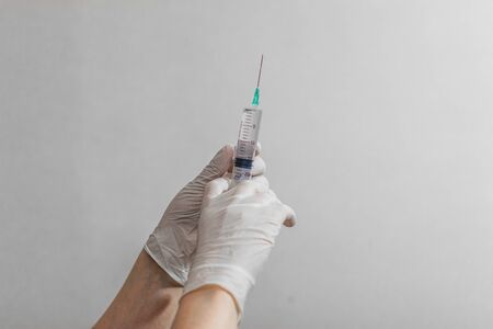 Hand wearing latex glove holding syringe with a medicine on white backgroundの写真素材