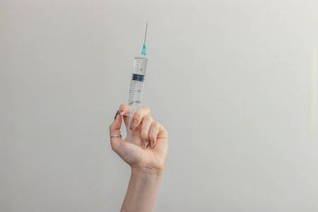 Syringe, medical injection in hand, palm or fingers. Medicine plastic vaccination equipment with needle. Nurse or doctor. Liquid drug or narcotic. Health care in hospital.の写真素材