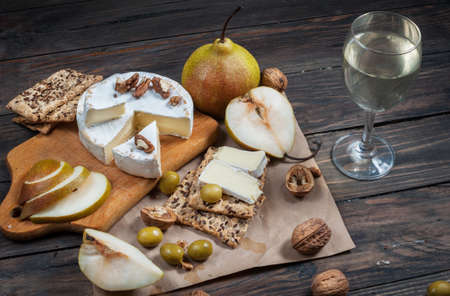Camembert cheese with walnuts, honey and pears on rustic table. Glass of white wine.の写真素材
