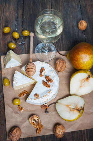 Camembert cheese with walnuts, honey and pears on rustic table. Glass of white wine.の写真素材