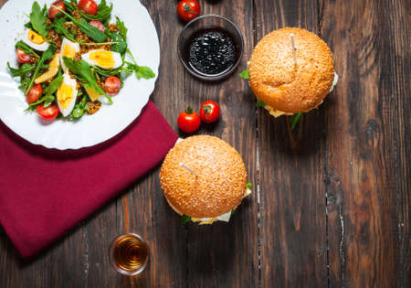 Fresh homemade burgers with a salad with arugula and alcohol on a dark background. View from above. Top viewの写真素材