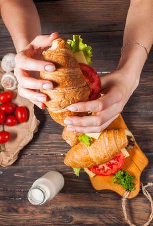 Croissant with vegetables in female hands. Sandwich with tomato, cheese, salad.の写真素材