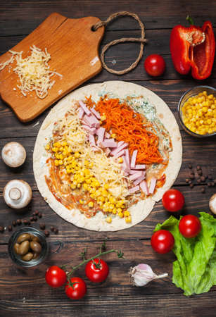 Cooking tortilla wraps with ham, corn, cheese, mushrooms and carrot on the wooden table.の写真素材
