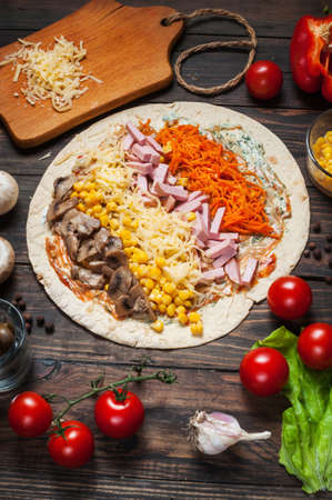 Cooking tortilla wraps with ham, corn, cheese, mushrooms and carrot on the wooden table.の写真素材