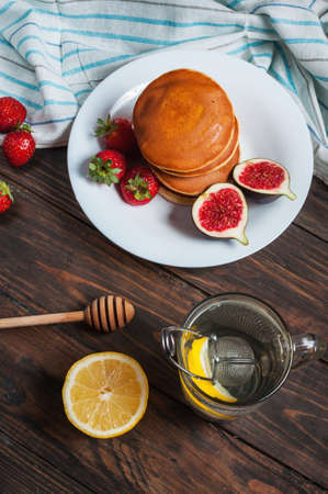 cup of tea and pancakes with figs, strawberries on white plate closeup.