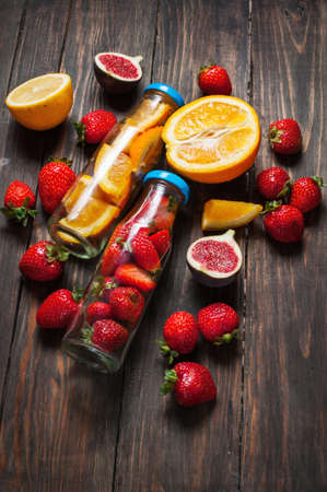 Bottle with sliced oranges and strawberries on wooden table, organic vegan drink.の写真素材