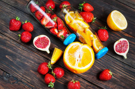 Bottle with sliced oranges and strawberries on wooden table, organic vegan drink.の写真素材