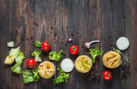 Italian food cooking ingredients. Pasta, tomatoes, onion on dark wooden background.の写真素材