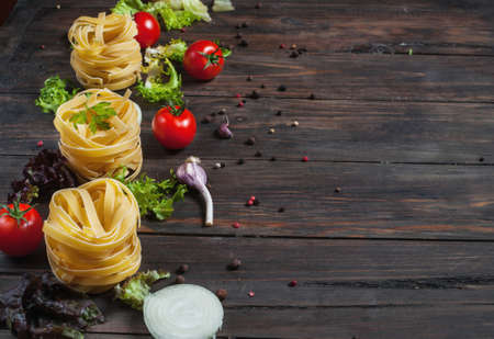 Italian food cooking ingredients. Pasta, tomatoes, onion on dark wooden background.の写真素材