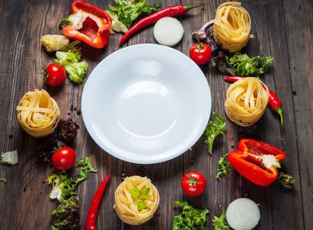 Ingredients for cooking spagetti, cherry tomatoes, pepper around a white plate place text, frame on wooden rustic background top view.の写真素材