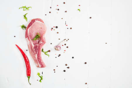Top view raw pork chop steak and garlic, chili pepper on white wooden background.の写真素材