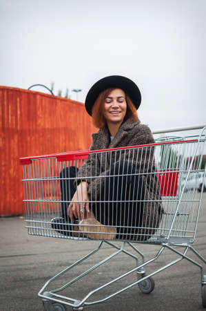 Fashion hipster cool girl in shopping cart having fun against the colorful orange wall.の写真素材