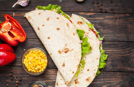 Sandwiches twisted roll Tortilla two pieces and vegetables on a wooden background.