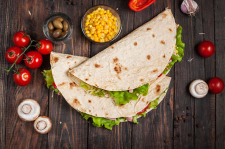 Sandwiches twisted roll Tortilla two pieces and vegetables on a wooden background.の写真素材