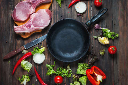 Raw pork steak with herbs, pepper and garlic around the pan place for text, frame on wooden rustic background top view.の写真素材