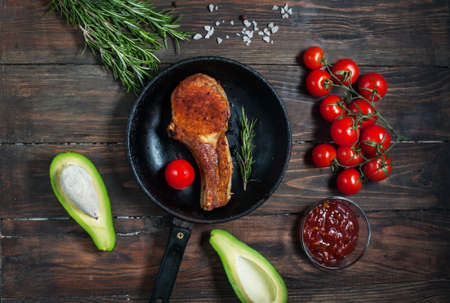 Steak in frying pan, avocado and cherry tomatoes on table.