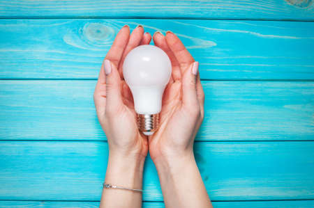 female hand selected led lamp of innovation electric lamp on blue wood background