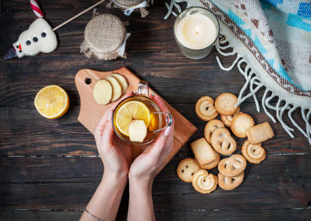 female hands holding cup black tea with lemon, ginger and cookies on dark wood.の写真素材