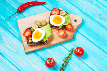 Sandwiches with olive, quail eggs, cherry tomatoes and potatoes on a wooden blueboard. Delicious healthy snack or Breakfast.の写真素材