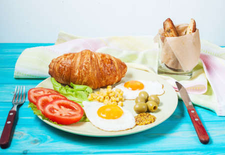 Breakfast on a wooden table. Fried eggs, tomatoes, croissant.の写真素材