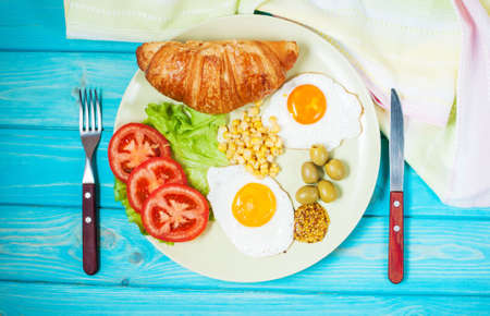 Breakfast on a wooden table. Fried eggs, tomatoes, croissant.の写真素材