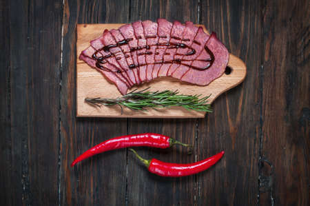Sliced ham, chilli pepper, rosemary on a wooden board.の写真素材