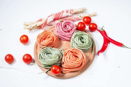 Colorful rolled pasta, cherry tomatoes and bacon on the white wooden background.の写真素材