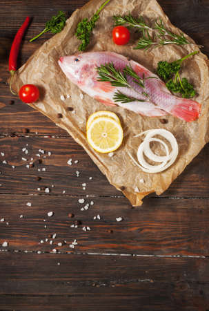 fresh tilapia on dark wooden textured background with fresh rosemary and lemon. Culinary...
