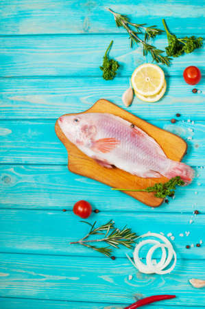 fresh tilapia on blue wooden textured background with fresh rosemary and lemon. Culinary...