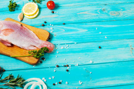 fresh tilapia on blue wooden textured background with fresh rosemary and lemon. Culinary mediterranean seafood.の写真素材