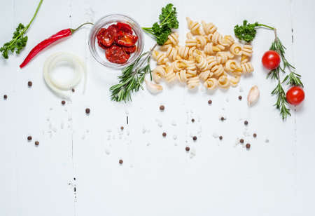 Background with pasta, tomatoes cherry and herb on white wooden table. Place for textの写真素材