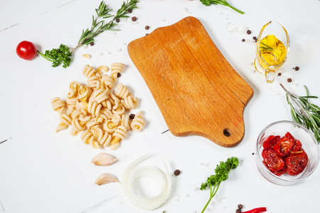 Background with pasta, tomatoes cherry and herb on white wooden tableの写真素材