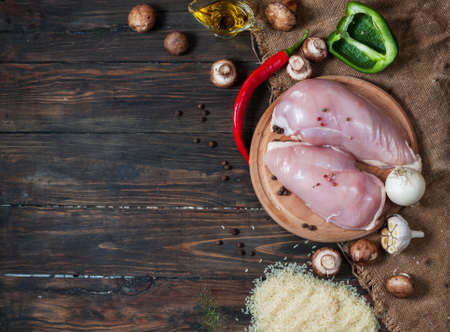 Chiken breast On a cutting board with herbs different fruits and vegetables on rustic wooden background top view.の写真素材