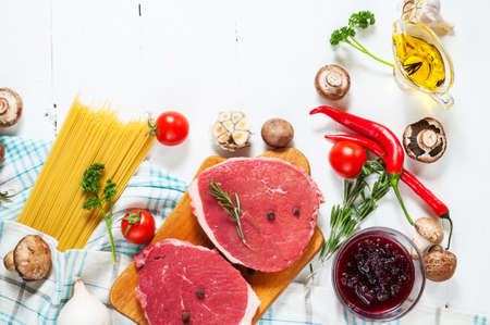 Raw beef steak with pasta, tomatoes, mushrooms and cheese on white table background, top view food conceptの写真素材