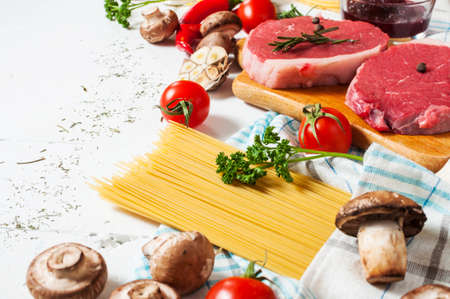 Raw beef steak with pasta, tomatoes, mushrooms and cheese on white table background, food conceptの写真素材