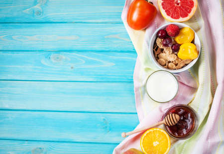 Bowl of healthy corn flakes breakfast cereal, milk and fruits on blue wood table. Top view