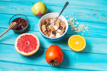 Bowl of healthy corn flakes breakfast cereal, milk and fruits on blue wood table.の写真素材