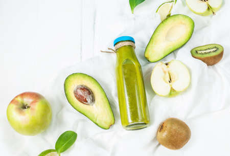 Green smoothie in bottl with avocado, apple and kiwi on white wooden background. Top view