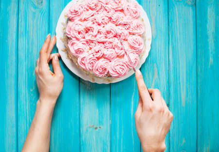 Woman's hands cut the cake with pink cream on blue wood background. Pink cake. Top view