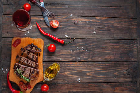 Grilled beef steak seasoned with spices served on a wooden board with fresh cherry tomato and red hot chili peppers.の写真素材