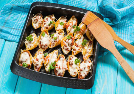 Italian pasta Conchiglioni Rigati stuffed with cheese and meat on blue wood table.の写真素材