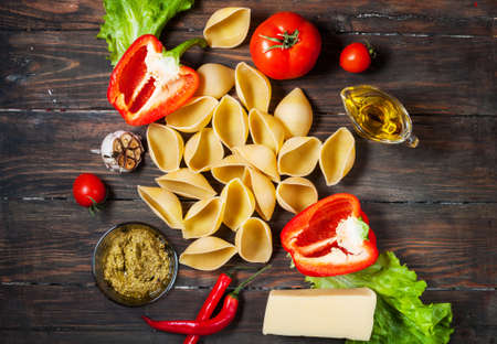 Ingredients for cooking pasta. Conchiglioni, cherry-tomatoes, cheese, oil, garlic, pepper on rustic wooden background, top viewの写真素材
