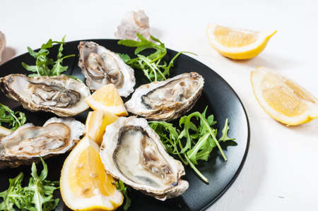 Oysters with lemon fruit on a black plate on a white wood tableの写真素材