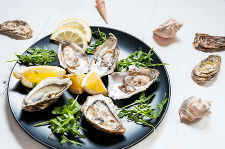 Oysters with lemon fruit on a black plate on a white wood tableの写真素材