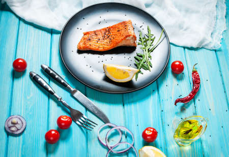 One piece of baked salmon with lemon on a black plate. Blue wood background.の写真素材