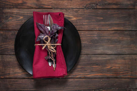 Black plate with fork,knife, napkin and basil on wooden table. Top viewの写真素材