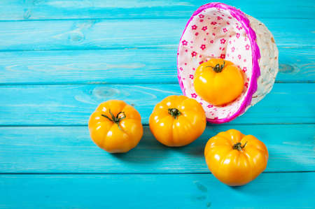 yellow tomatoes in a wicker basket on wood background. Top viewの写真素材